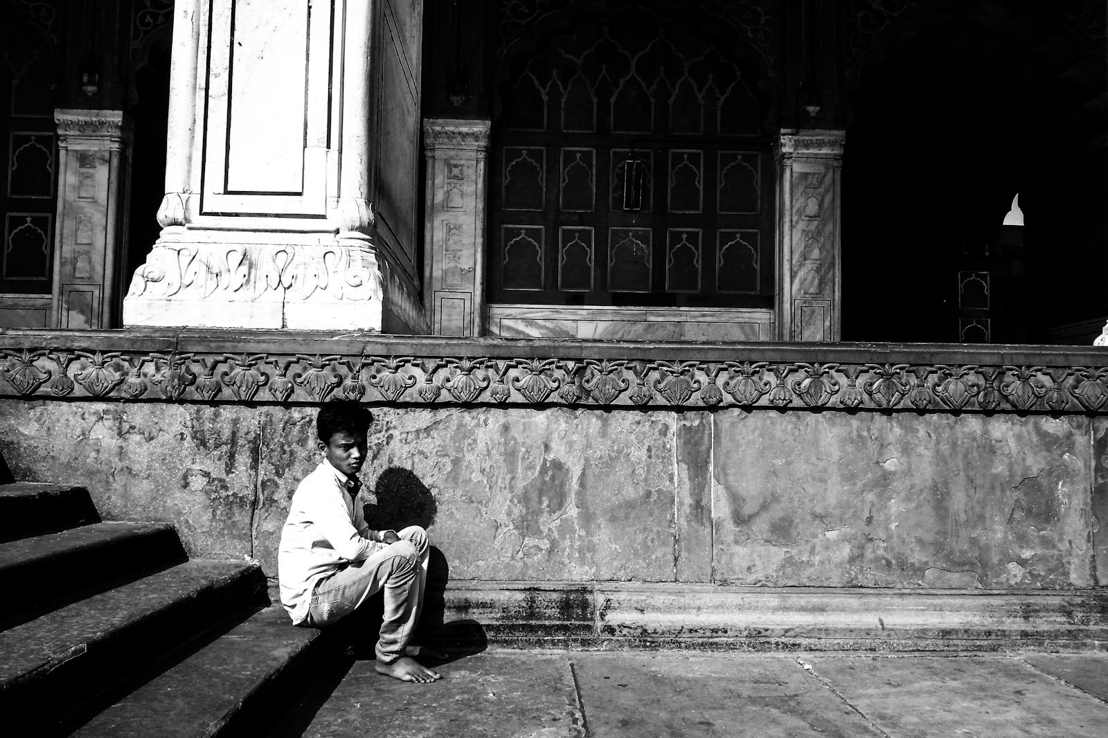 A young boy sitting on historic steps in Delhi, conveying solitude and contemplation.