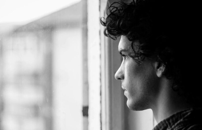 Profile portrait of a young man looking thoughtfully out of a window, in black and white.