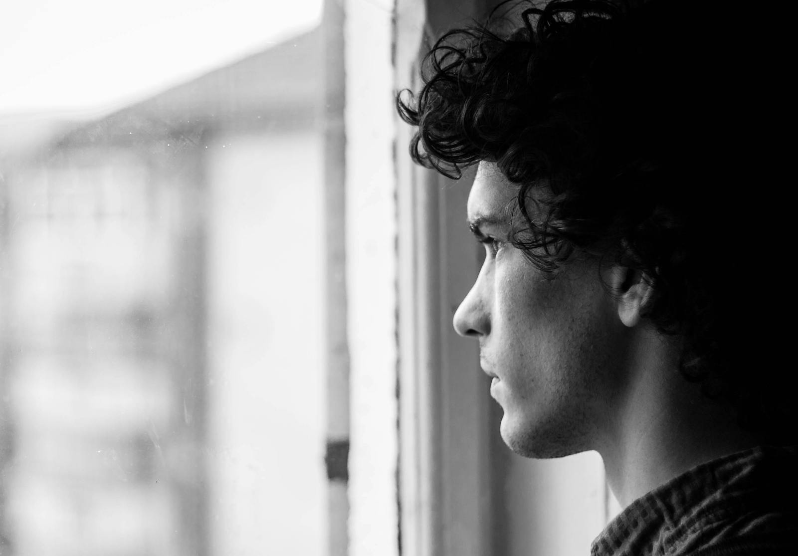 Profile portrait of a young man looking thoughtfully out of a window, in black and white.