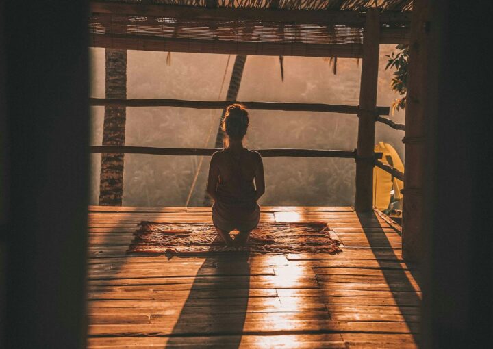 woman meditating on floor with overlooking view of trees