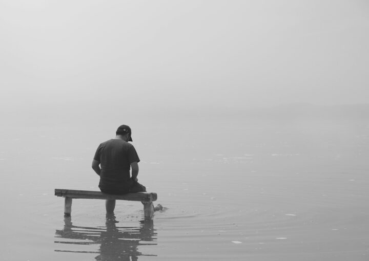 grayscale photo of man sitting on dock