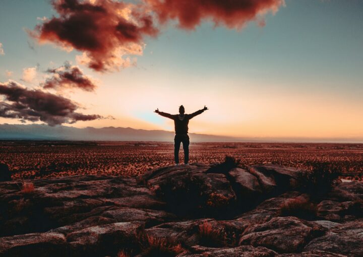 person standing on rock raising both hands