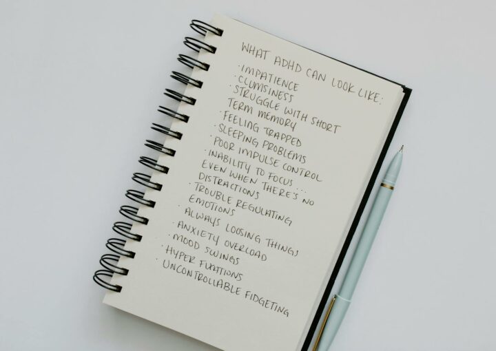 Notebook open with handwritten list of ADHD symptoms, featuring a pen alongside.