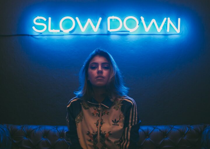 woman sitting on brown sofa under slow down neon signage